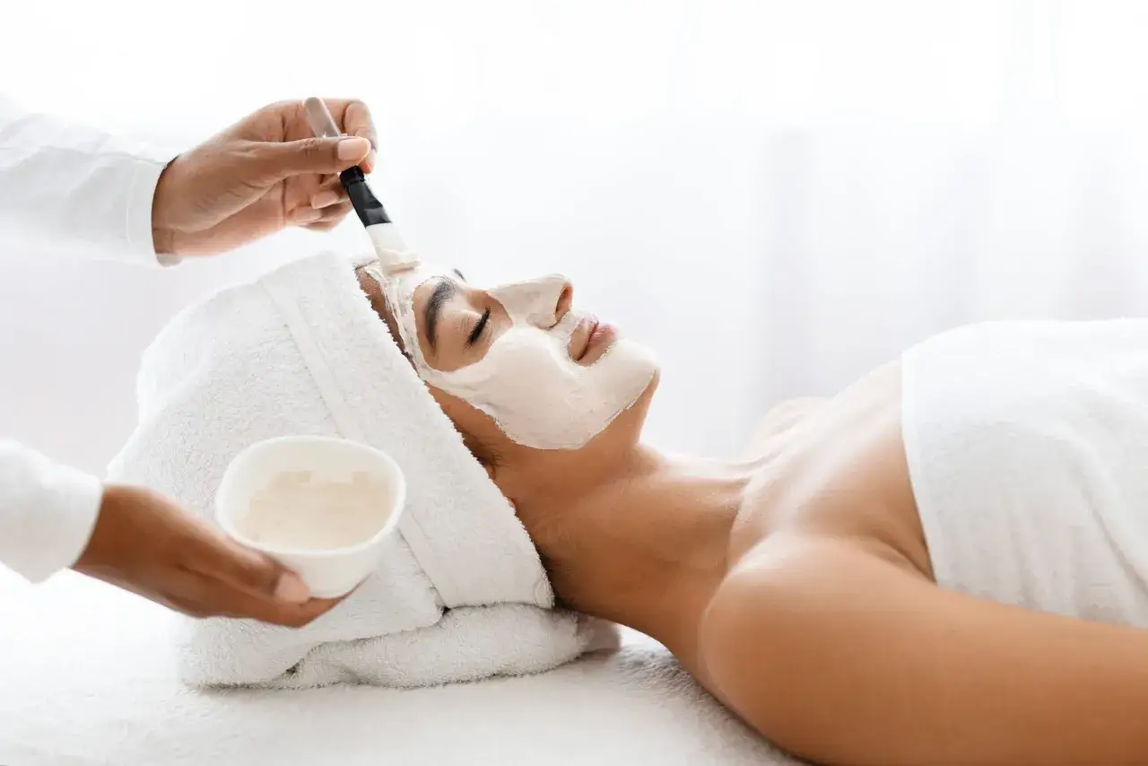 Une esthéticienne applique un masque apaisant sur le visage d'une femme lors d'un soin de nettoyage de peau.