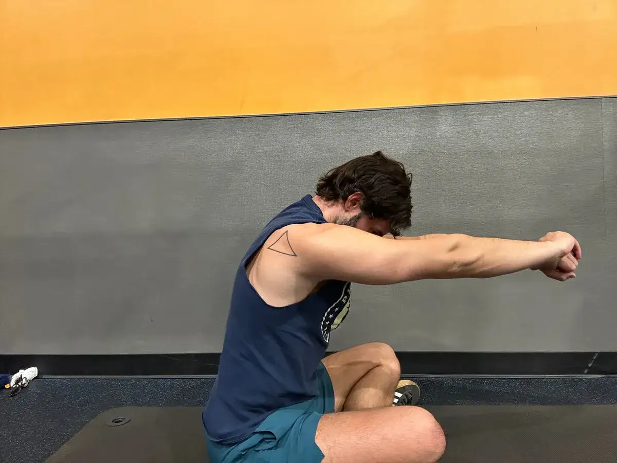 Un homme s'étire, bras tendus, travaillant son grand rhomboïde. Un tatouage en forme de triangle orne son épaule.