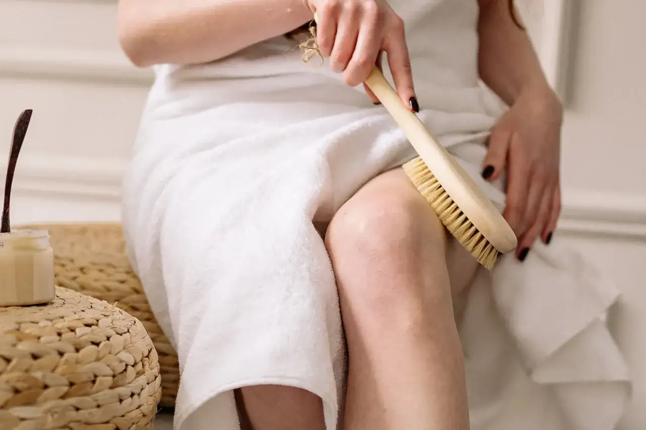 Une femme utilise une brosse pour le corps, mais attention au brossage à sec danger : une peau irritée peut en résulter.