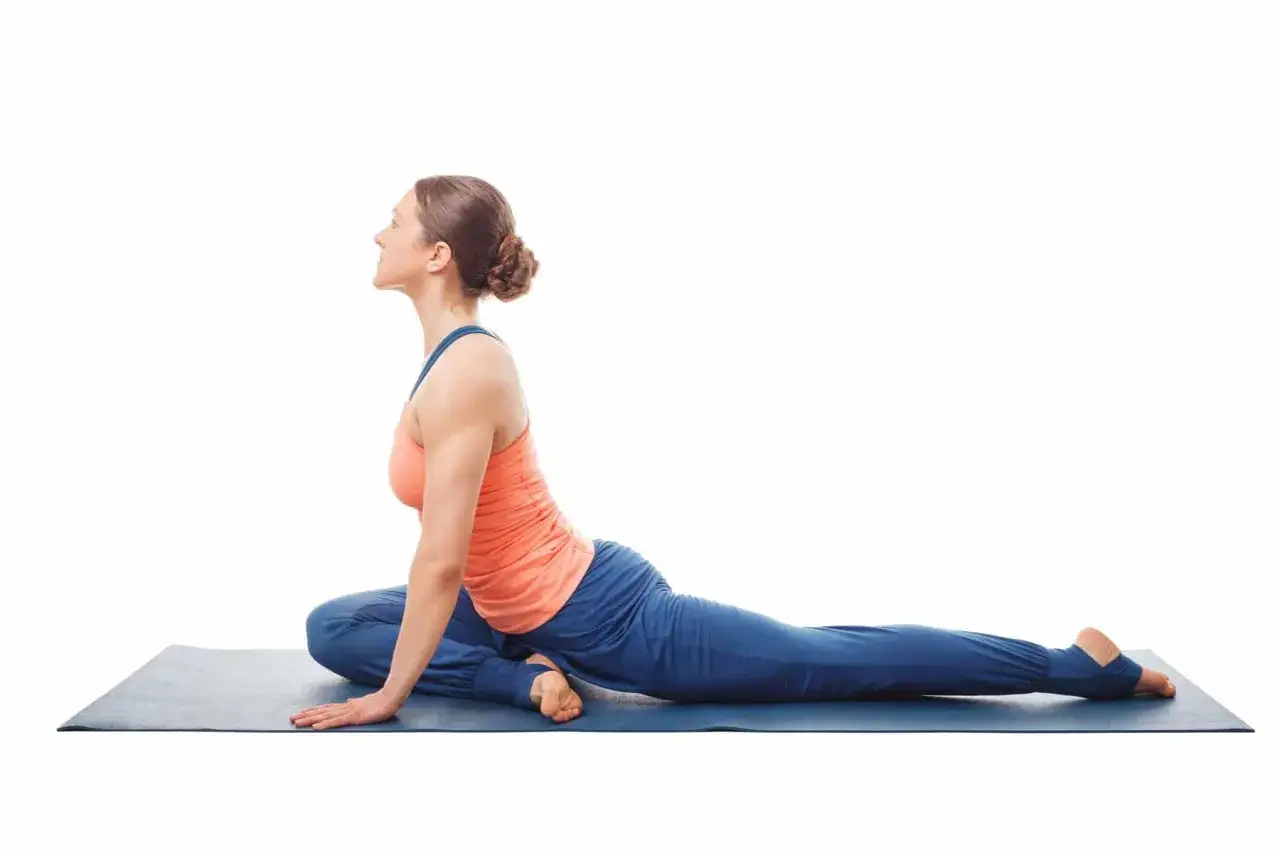 Femme en posture du pigeon sciatique sur un tapis de yoga bleu, le corps penché en avant, une jambe pliée sous elle, l'autre étendue derrière.
