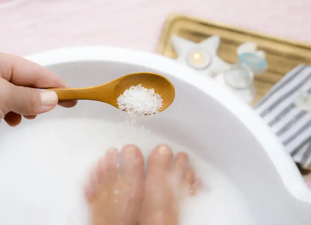 Une cuillère en bois verse du gros sel et du bicarbonate dans un bain de pied pour un moment de détente.