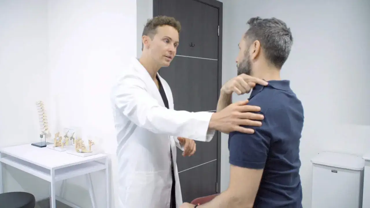 Un médecin examine un patient souffrant d'une nuque bloquée, pointant vers la zone douloureuse.