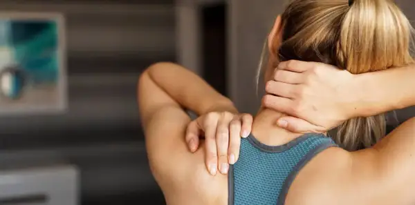 Une femme se masse le cou et les épaules, cherchant un soulagement pour ses trapezes tendus.