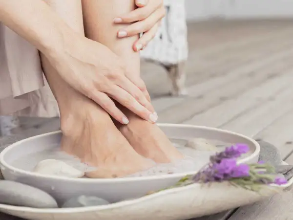 Détente avec un bain de pied maison, pieds dans l'eau savonneuse, galets et lavande.