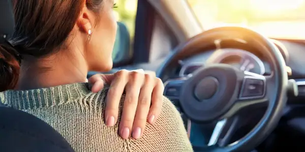 Femme au volant, main sur l'épaule, souffrant de tendinite. La conduite de voiture peut être douloureuse.