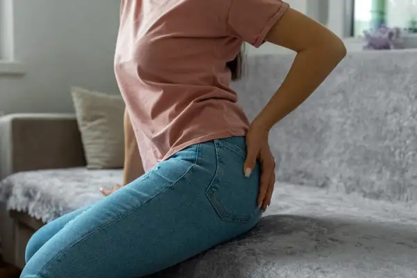 Femme assise sur un canapé, main sur la hanche, possiblement une douleur au piriforme.