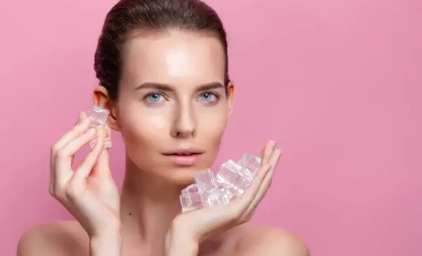 Une femme au visage frais tient des glaçons dans ses mains, un geste rafraîchissant pour la peau.