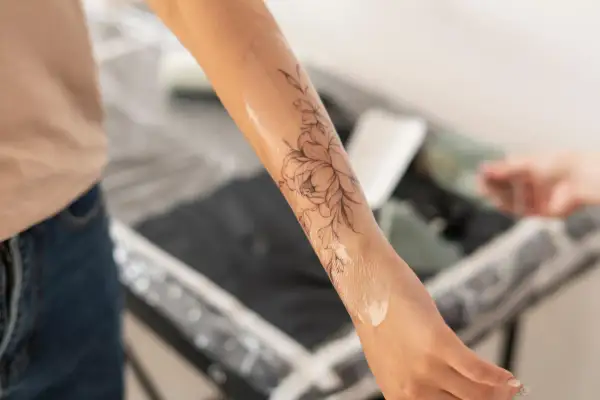 Application d'une crème sur un tatouage floral pour favoriser la cicatrisation. La peau est légèrement brillante.