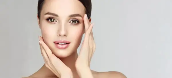 Visage de femme aux mains délicates caressant sa peau, évoquant un soin de nettoyage de peau parfait.