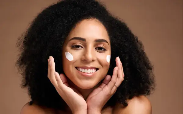 Une femme souriante avec des touches de crème sur les joues, profitant des bienfaits du beurre de karité visage pour une peau douce et hydratée.