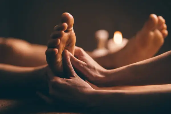 Mains massant un pied, éclairé par des bougies. Une invitation à découvrir ce qu'est la réflexologie plantaire.