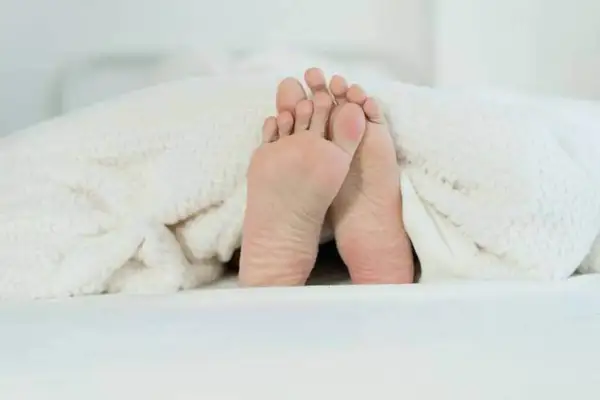 Pieds sous une couverture douillette, prêts pour un point massage pied pour dormir paisiblement.