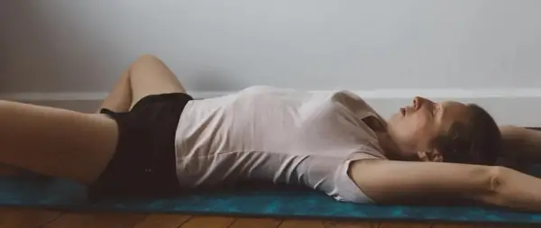 Femme allongée sur un tapis, jambes écartées, bras derrière la tête. Une posture pour comment détendre les adducteurs en douceur.